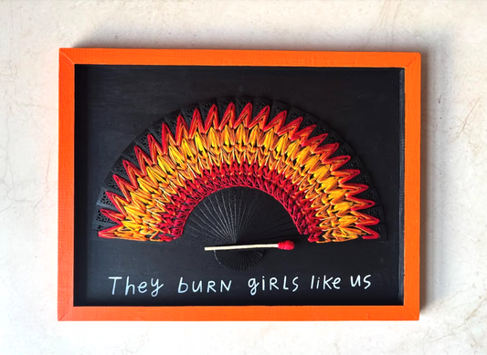 Framed artwork with a matchstick and colorful embroidered flame fan on a black background. Hand lettering.